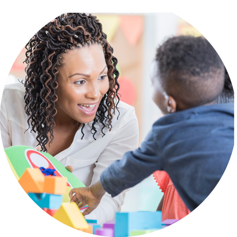 Woman playing blocks with small child in school setting