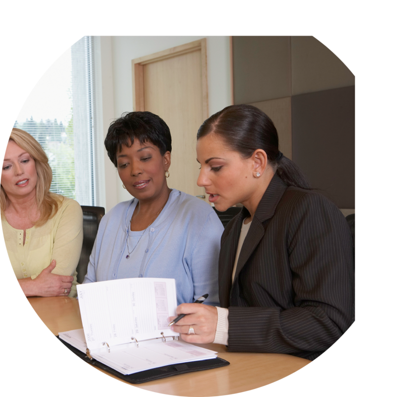 Three women in an office setting sitting around a table reviewing a calendar