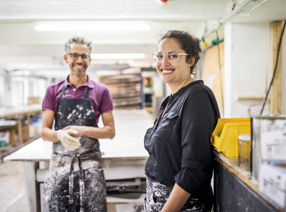 Man and woman in paint covered clothes smiling in a factory setting