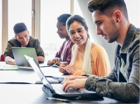 Group of young men and women sitting together at table looking at computers in office setting